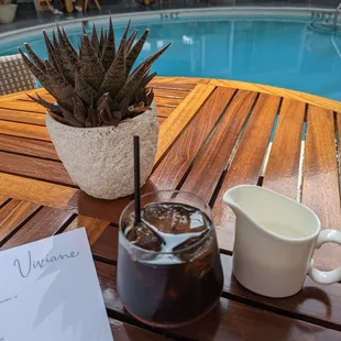 a cup of coffee and a pitcher on a table next to a pool