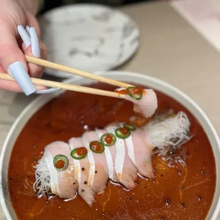 a person holding chopsticks over a bowl of soup