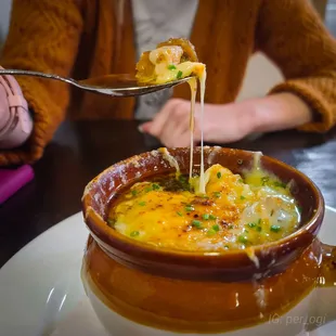 a bowl of soup with cheese being lifted by a fork