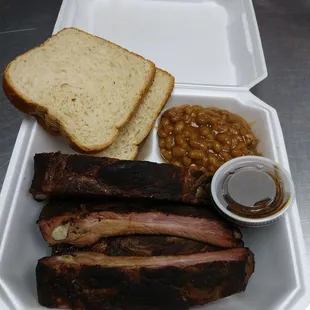 ribs, baked beans, and bread in a styrofoam container