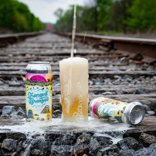 a glass of beer and a can of beer on a railroad track