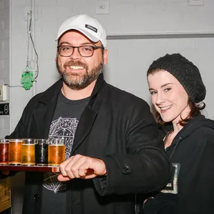 a man and a woman holding a tray of beer