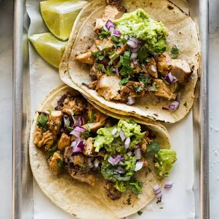 two chicken tacos with guacamole and lime wedges