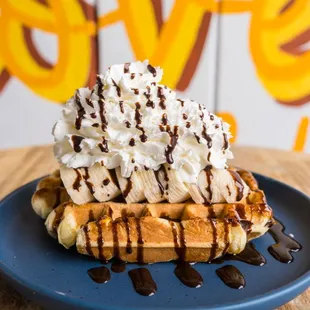 a waffle topped with whipped cream and chocolate syrup