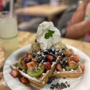 Two waffles with a scoop of açaí and vanilla ice cream, fresh berries and kiwis and bananas and fresh whipped cream.