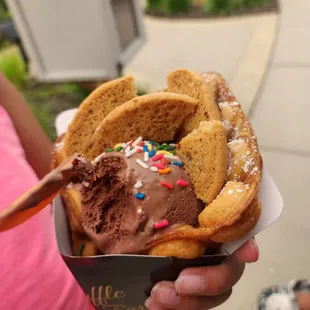 a person holding a waffle with chocolate frosting and sprinkles