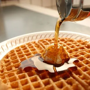 a waffle being drizzled with syrup