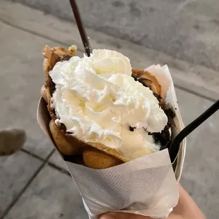 a hand holding a waffle - licious with whipped cream on top