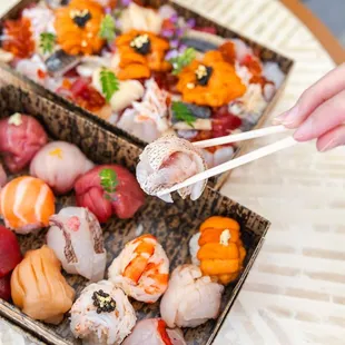 a person holding chopsticks over a box of sushi