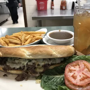 Philly cheesesteak sandwich with lettuce and tomato added on the side, French fries with beef gravy.