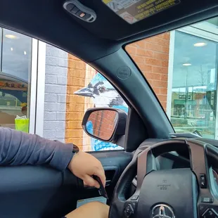 a woman sitting in a car with her hand on the steering wheel