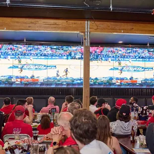 a crowd of people watching a basketball game on a big screen