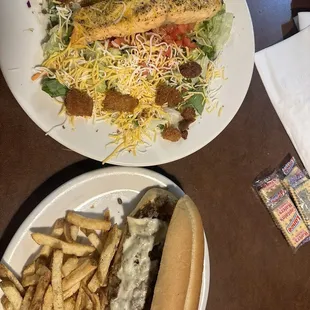 Philly cheesesteak with fries and a salmon salad.