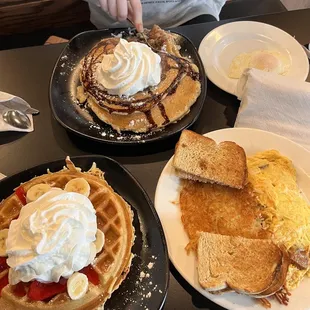 two plates of waffles with whipped cream and strawberries