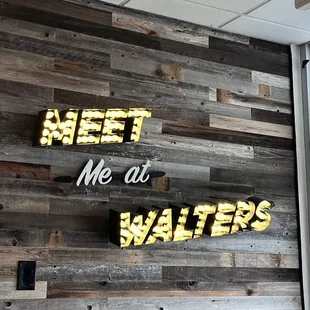 a wooden wall with a neon sign that says meet me at walters