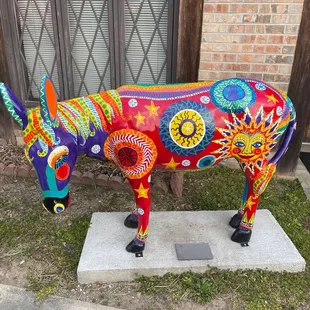 a colorful cow statue in front of a brick building