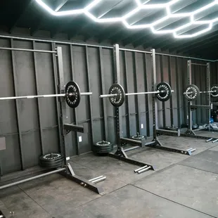 Weight room with squat racks with olympic style weights, hex bars, and dumbbells for strength and power.