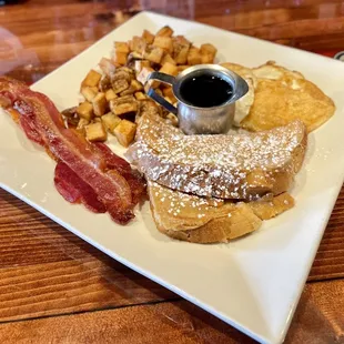 a plate of french toast, bacon, and hash browns