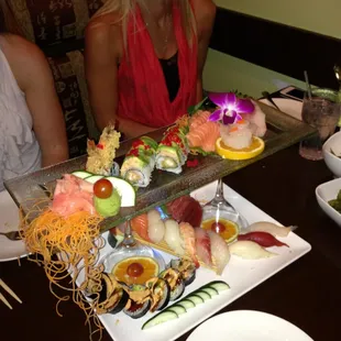 a woman sitting at a table with a platter of sushi
