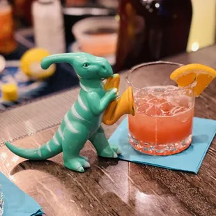 a dinosaur figurine next to a drink on a table
