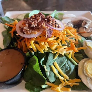 a salad with hard boiled eggs, spinach, cheese, and bacon