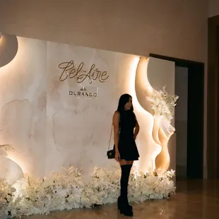 a woman standing in front of a wall of flowers