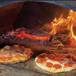 two pizzas cooking in a brick oven