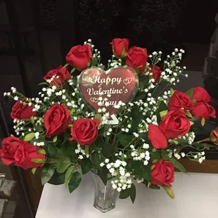 a vase of red roses with a happy valentine&apos;s day sign