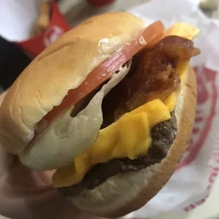a hand holding a hamburger with bacon and cheese