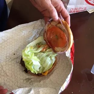 a hand holding a sandwich with lettuce and tomato