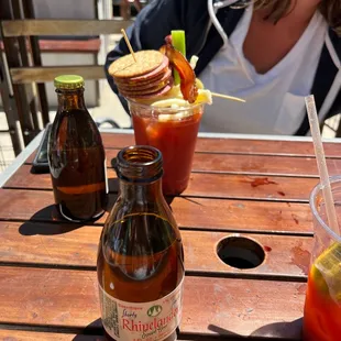 a woman sitting at a table with a bottle of beer and a bloody drink
