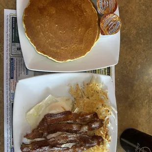 Two pancakes, hash browns and eggs over easy and bacon.