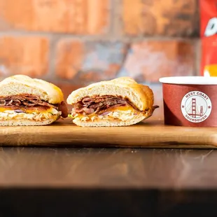two sandwiches on a cutting board with a cup of chips