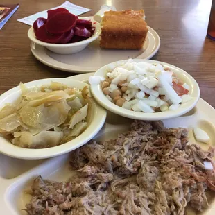 a plate of pulled pork, coleslaw, pickles, and bread