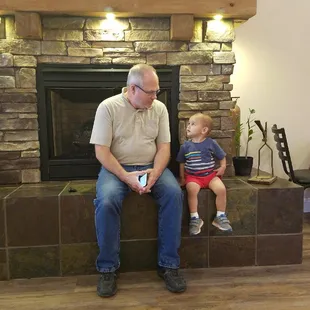 a man and a young boy sitting on a fireplace