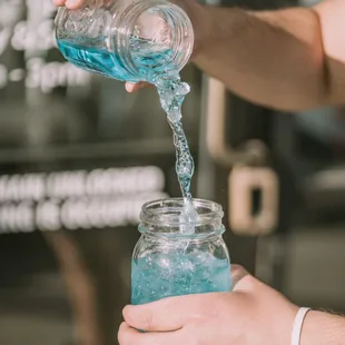 a person pouring blue liquid into a jar