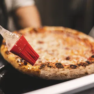 a pizza being brushed with a spatula