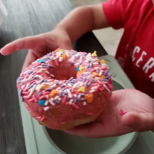 a child holding a pink frosted donut with sprinkles