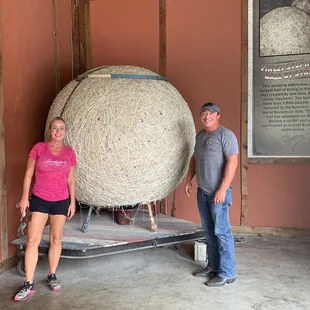 a man and a woman standing in front of a large ball of yarn
