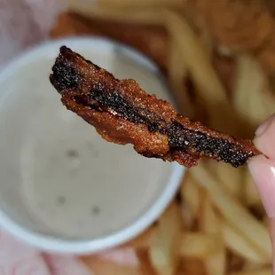 a hand holding a piece of bacon
