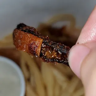 a hand holding a piece of bacon