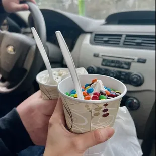 a person holding two cups of ice cream