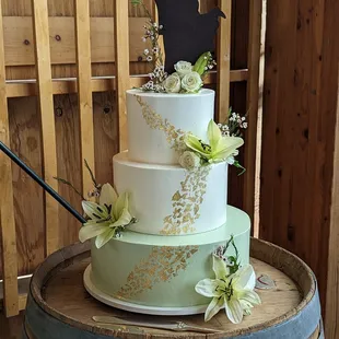 Buttercream cake, with sage green bottom and white top tiers. Accented with edible gold leaf and fresh flowers.