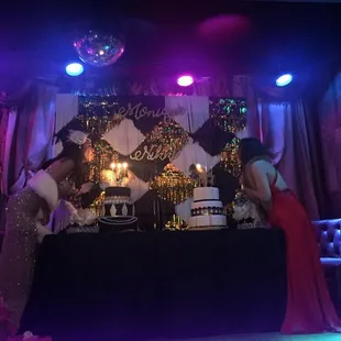 a woman in a red dress standing in front of a table with a cake on it
