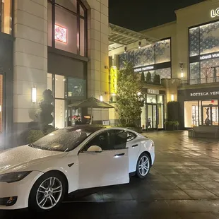 a white tesla model s parked in front of a luxury store