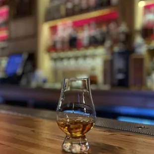 a glass of whisky sitting on a bar