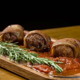 bacon wrapped in tomato sauce and garnished with a sprig of rosemary
