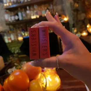a person holding a book in front of a pile of oranges