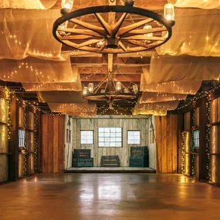The rustic charm of this barn, accentuated by warm string lights and elegant drapes, offers a cozy and customizable venue for a wedding.