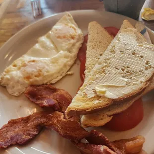 Two eggs over medium, crispy bacon, sore dough bread and tomatoes.